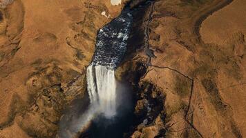 Antenne Aussicht von enorm Kaskade im Island, Fluss fließen Laufen Nieder von natürlich gefroren Hügel. schön nordisch Skgafoss Wasserfall fließend aus Klippen Bildung tolle isländisch Landschaft. schleppend Bewegung. foto