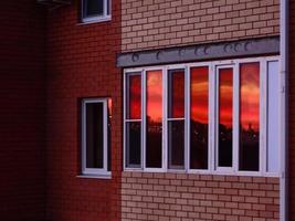 Reflexion des Sonnenuntergangs mit einem orangefarbenen Himmel in den Fenstern eines Backsteinhauses foto