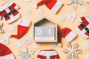 Draufsicht auf Holzkalender mit Weihnachtsschmuck und Weihnachtsmützen auf orangefarbenem Hintergrund. Der erste Januar. fröhliches Urlaubskonzept foto