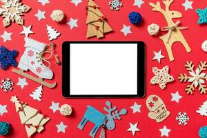Draufsicht auf digitales Tablet, Weihnachtsspielzeug und Dekorationen auf rotem Weihnachtshintergrund. neujahrszeitkonzept foto