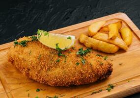 paniert Schnitzel mit Französisch Fritten auf ein Schneiden Tafel foto