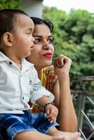 liebend Mama Tragen von ihr Baby beim Zuhause Balkon. hell Porträt von glücklich Mama halten Kind im ihr Hände. Mutter mit ihr wenig 1 Jahr alt Sohn. foto