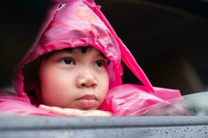 asiatisch Mädchen tragen ein Rosa Regenjacke im das Wagen. machen ein traurig Gesicht wann Ihre Eltern machen Sie warten während Einkaufen. foto