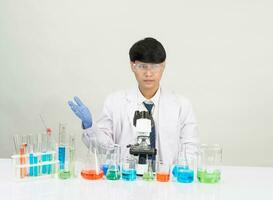 Porträt asiatisch Mann Schüler Wissenschaftler tragen ein Arzt Kleid im das Labor suchen Hand beim Chemiker. verursacht durch Mischen Reagenzien im wissenschaftlich Forschung Laboratorien mit Prüfung Röhren und Mikroskop auf das Tabelle foto