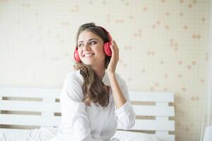 Schöne Frau, die morgens Musik hört, die zu Hause auf dem Bett sitzt foto