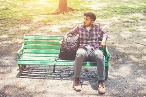 junger Hipster-Mann mit Rucksack neben dem Sitzen auf einer Holzbank. foto