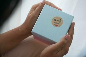 Frauen Hand Putten ein danken Sie Aufkleber auf ein Geschenk Box foto
