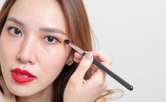 Porträt schöne asiatische Frau mit Make-up-Augenbürste auf weißem Hintergrund foto