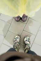Draufsicht auf zwei Paar weiblicher Füße, die an einem regnerischen Tag in Pfützen stehen foto