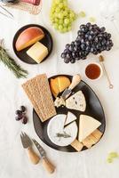 Käseplattensortiment serviert mit Honig, Weintrauben, Brot und Rosmarin foto