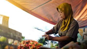 Gemüse Verkäufer Muslim Indonesien Frauen mit Kopftuch ist Portion Kunden im das Markt. Lebensmittel Verkäufer. Verkäufer Frauen im das traditionell Markt foto