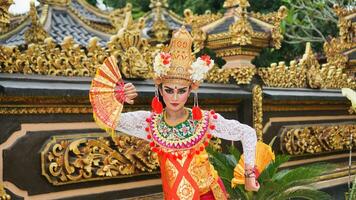 Mädchen tragen balinesisch traditionell Kleid mit ein Tanzen Geste auf balinesisch Tempel Hintergrund mit Handheld Fan, Krone, Schmuck, und Gold Ornament Zubehör. balinesisch Tänzer Frau Porträt foto