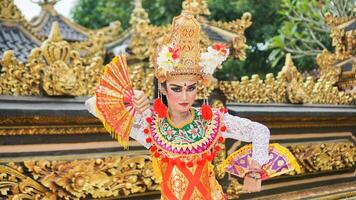 Mädchen tragen balinesisch traditionell Kleid mit ein Tanzen Geste auf balinesisch Tempel Hintergrund mit Handheld Fan, Krone, Schmuck, und Gold Ornament Zubehör. balinesisch Tänzer Frau Porträt foto