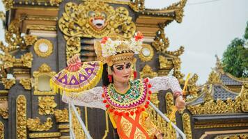 Mädchen tragen balinesisch traditionell Kleid mit ein Tanzen Geste auf balinesisch Tempel Hintergrund mit Handheld Fan, Krone, Schmuck, und Gold Ornament Zubehör. balinesisch Tänzer Frau Porträt foto