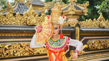 Mädchen tragen balinesisch traditionell Kleid mit ein Tanzen Geste auf balinesisch Tempel Hintergrund mit Handheld Fan, Krone, Schmuck, und Gold Ornament Zubehör. balinesisch Tänzer Frau Porträt foto