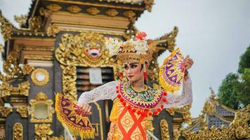 Mädchen tragen balinesisch traditionell Kleid mit ein Tanzen Geste auf balinesisch Tempel Hintergrund mit Handheld Fan, Krone, Schmuck, und Gold Ornament Zubehör. balinesisch Tänzer Frau Porträt foto