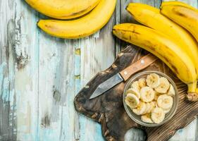 Bananen und Banane Scheiben im ein Glas Schüssel auf ein alt Schneiden Tafel. foto