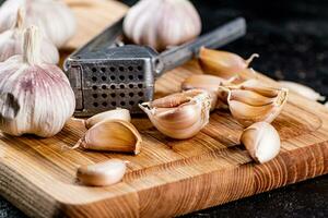 Nelken von Knoblauch auf ein Schneiden Tafel mit ein Knoblauch Drücken Sie. foto