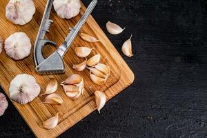 Nelken von Knoblauch auf ein Schneiden Tafel mit ein Knoblauch Drücken Sie. foto