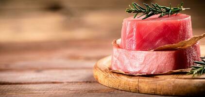 ein Steak von roh Thunfisch auf ein Schneiden Tafel mit ein Zweig von Rosmarin. foto