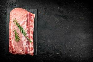 ein Stück von roh Schweinefleisch auf ein Stein Tafel mit ein Zweig von Rosmarin. foto