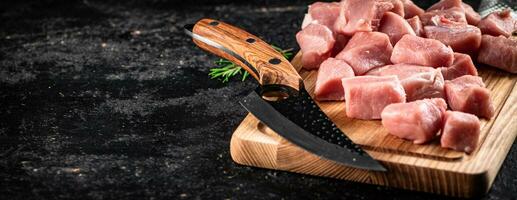 Stücke von roh Schweinefleisch auf ein hölzern Schneiden Tafel mit ein Messer. foto