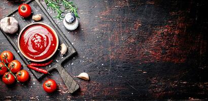 Tomate Soße auf ein Schneiden Tafel mit rot Pfeffer, Knoblauch und Rosmarin. foto