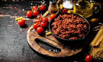 Bolognese Soße auf ein Schneiden Tafel mit Kirsche Tomaten und trocken Pasta. foto