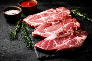 roh Schweinefleisch Steak auf ein Stein Tafel mit Tomate Soße, Rosmarin und Gewürze. foto