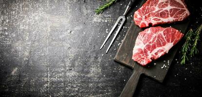 roh Schweinefleisch Steak auf ein Schneiden Tafel mit Rosmarin. foto