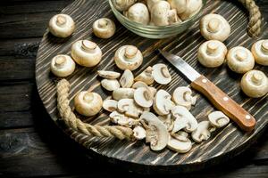 Pilze im ein Schüssel und Stücke von Pilze auf ein Tablett mit ein Messer. foto
