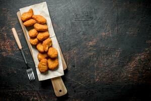 Hähnchen Nuggets auf Schneiden Tafel mit Papier und Gabel. foto
