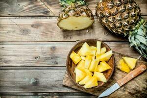 Stücke von duftend Ananas im ein Schüssel auf ein Schneiden Tafel mit ein Messer. foto