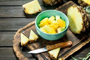 Stücke von reif Ananas im ein Schüssel auf ein Schneiden Tafel mit ein Messer. foto