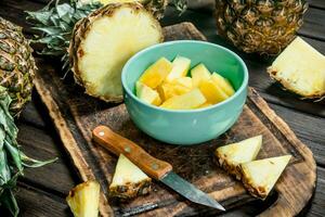 Stücke von reif Ananas im ein Schüssel auf ein Schneiden Tafel mit ein Messer. foto