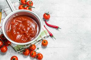 Tomate Soße im ein Topf auf ein Serviette mit ein Chili Pfeffer und Kirsche Tomaten. foto