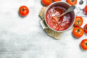 Tomate Soße im ein Topf mit ein Löffel auf Papier und reif Tomaten. foto