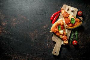 Scheiben von hausgemacht Pizza auf ein Schneiden Tafel mit Chili, Tomaten und Rosmarin. foto