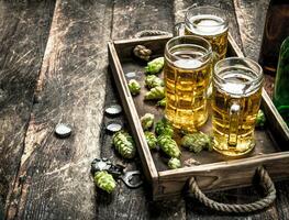 frisch Bier im Brille mit Grün Hopfen auf ein alt Tablett. foto