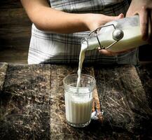 Frau gießt frisch Kuh Milch in ein Glas. foto