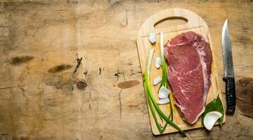 ein Stück von roh Fleisch mit ein Metzger Messer und ein Zwiebel. foto