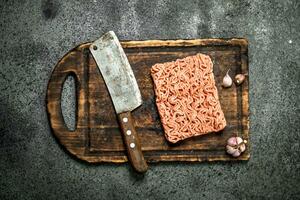 frisch gehackt Fleisch mit ein alt Beil und Knoblauch auf ein Schneiden Tafel. foto