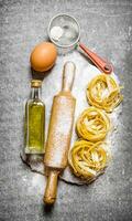 Pasta mit Olive Öl, Sieb, rollen Stift und Mehl auf ein Stein Stand. foto