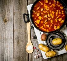 gedünstet Kartoffeln mit Fleisch und Gewürze im ein elektrisch Kocher auf hölzern Hintergrund . kostenlos Raum zum Text. foto