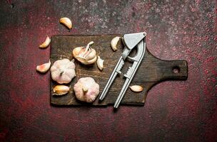 duftend Knoblauch mit ein Drücken Sie Werkzeug auf ein hölzern Tafel. auf rustikal Hintergrund. foto