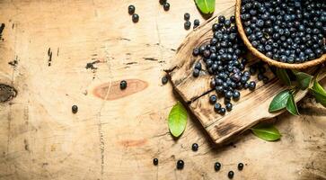 wild Blaubeeren im ein Tasse mit Blätter.auf hölzern Tisch. foto