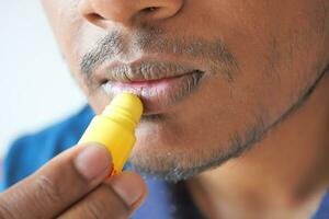 junger Mann, der feuchtigkeitsspendenden Lippenbalsam auf die Lippen aufträgt foto