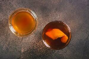 schließen oben von schwer alkoholisch braun Butter Cocktail mit Orange Zitrusschale im ein Glas oben Aussicht foto