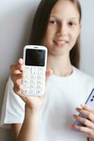 Weiß Druckknopf Telefon im das Hand von ein Mädchen mit ein Smartphone Vertikale Aussicht foto