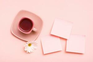 das Konzept ist Rosa. Rosa trinken im ein Kaffee Tasse, Blatt zum Schreiben und Chrysantheme auf ein Rosa Hintergrund. oben Sicht. Kopieren Raum foto